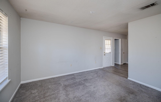 empty room with a textured ceiling and dark colored carpet