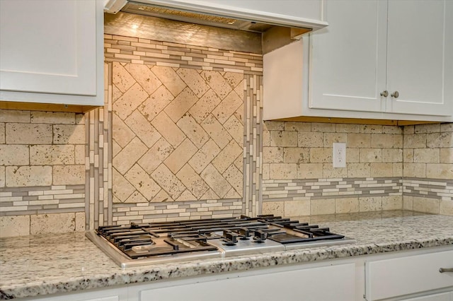 kitchen with stainless steel gas stovetop, light stone countertops, white cabinets, and decorative backsplash