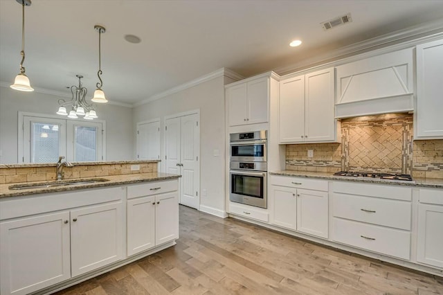 kitchen with appliances with stainless steel finishes, decorative light fixtures, sink, white cabinets, and light stone counters