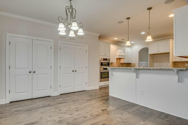 kitchen featuring white cabinetry, double oven, crown molding, and a kitchen bar