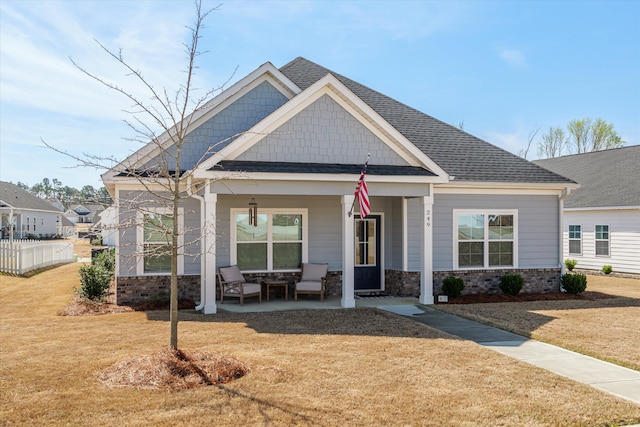 craftsman-style home featuring a shingled roof, a front lawn, fence, a porch, and stone siding