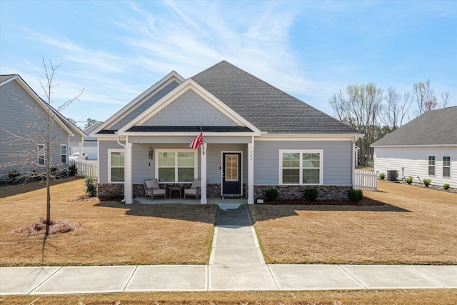 craftsman inspired home with central AC unit, fence, roof with shingles, covered porch, and a front lawn