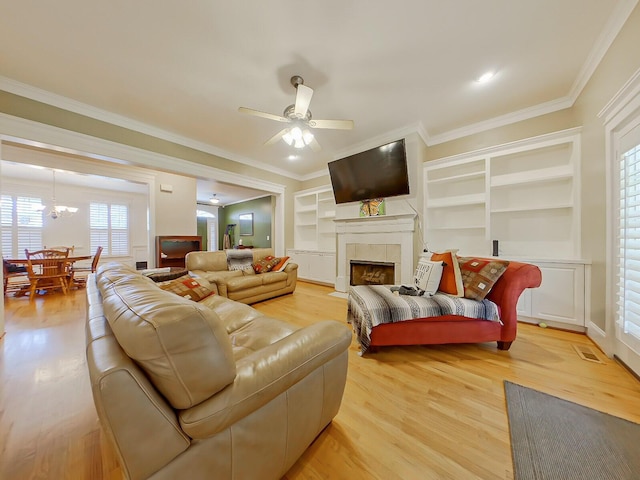 living area with light wood-style flooring, a tile fireplace, ceiling fan with notable chandelier, and ornamental molding