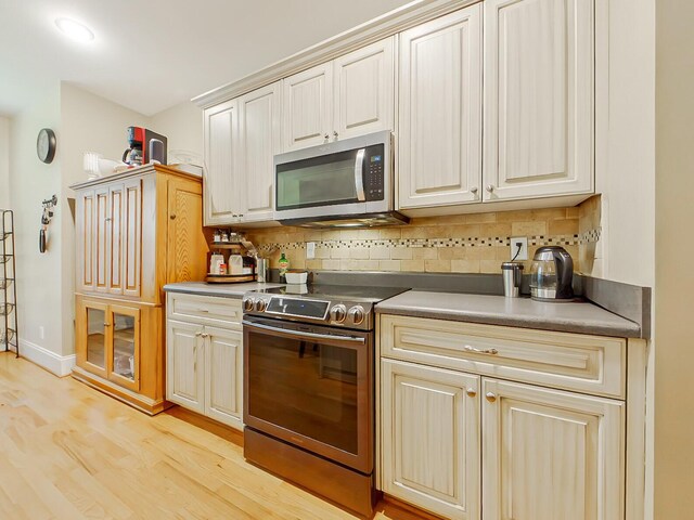 kitchen featuring decorative backsplash, baseboards, light wood-style floors, and appliances with stainless steel finishes