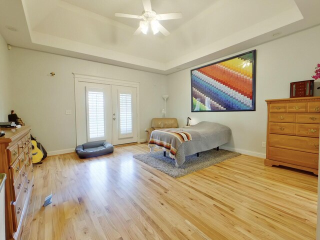 bedroom with a raised ceiling, access to outside, light wood-style floors, and baseboards