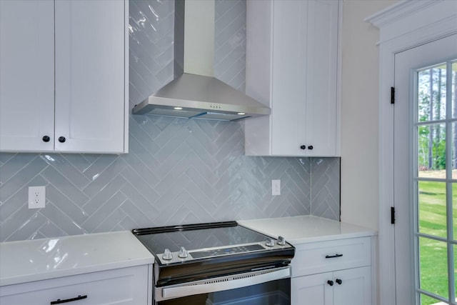 kitchen featuring wall chimney exhaust hood, stainless steel range with electric stovetop, white cabinets, and decorative backsplash