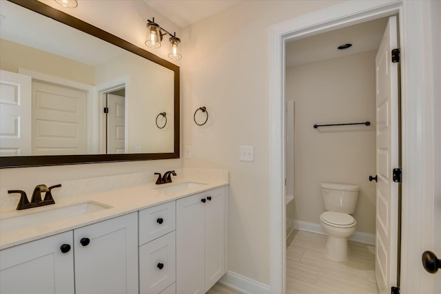 bathroom with baseboards, toilet, double vanity, and a sink