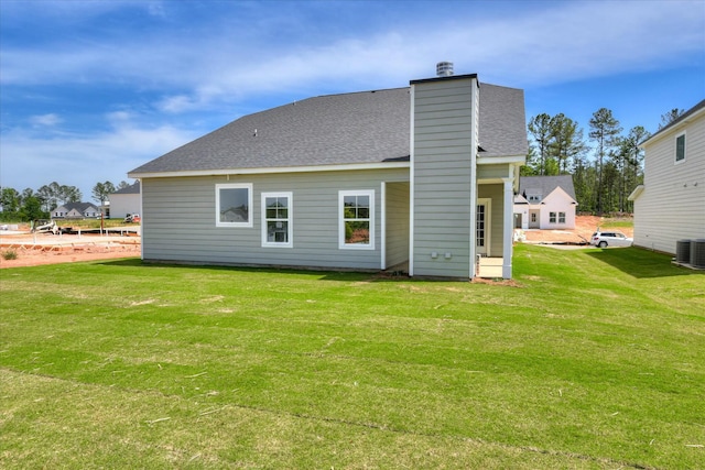 back of property featuring a chimney, central AC unit, a yard, and a shingled roof