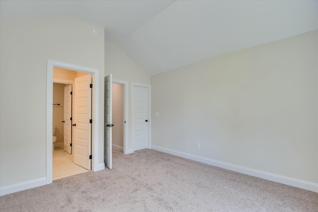 unfurnished bedroom with baseboards, ensuite bath, carpet floors, and vaulted ceiling