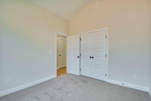 unfurnished bedroom with lofted ceiling, a closet, carpet, and baseboards