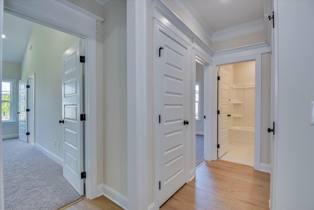hallway with baseboards, ornamental molding, light colored carpet, and light wood-style flooring
