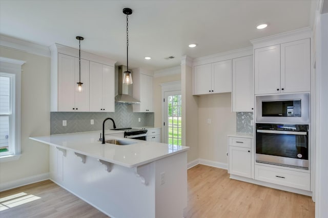 kitchen with a sink, stainless steel appliances, light countertops, wall chimney range hood, and baseboards