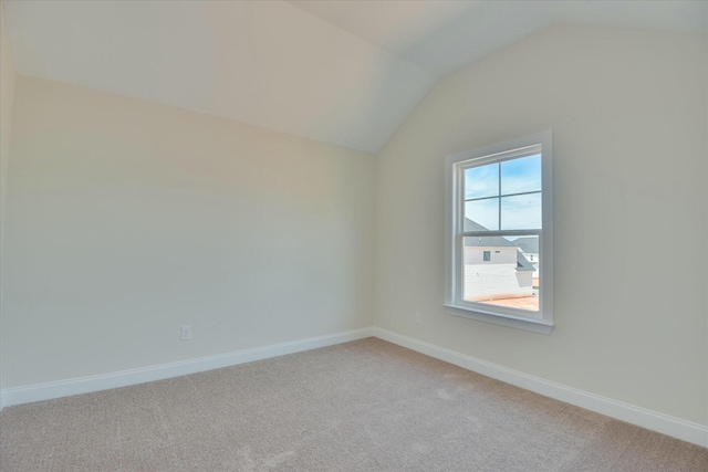 spare room with baseboards, light carpet, and vaulted ceiling