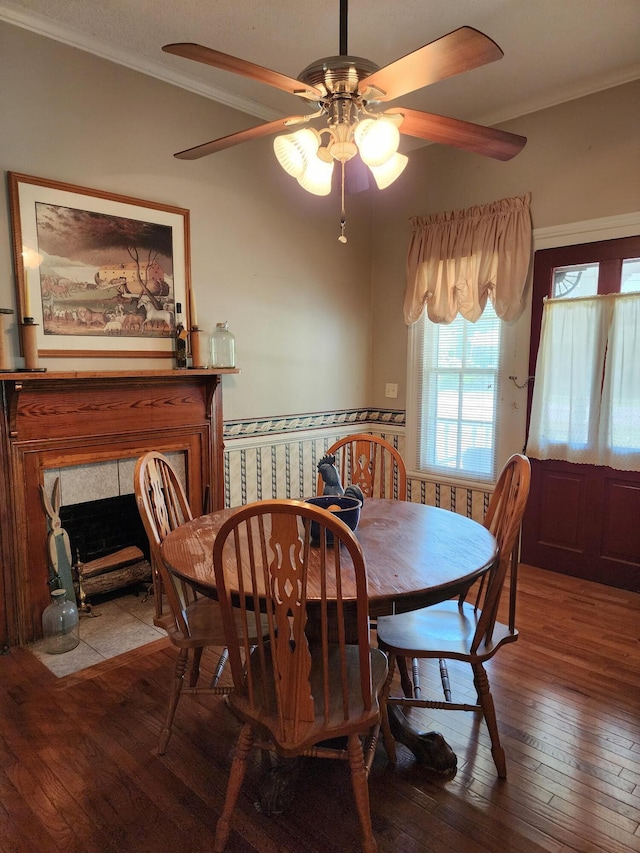 dining area with a tile fireplace, ceiling fan, hardwood / wood-style floors, and ornamental molding