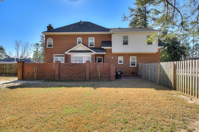 back of house with a fenced backyard, a chimney, a lawn, and brick siding