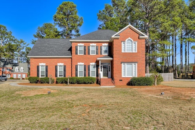 colonial inspired home with crawl space, a shingled roof, a front lawn, and brick siding