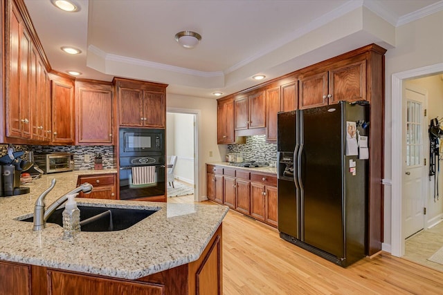 kitchen with a raised ceiling, light stone counters, a peninsula, black appliances, and a sink