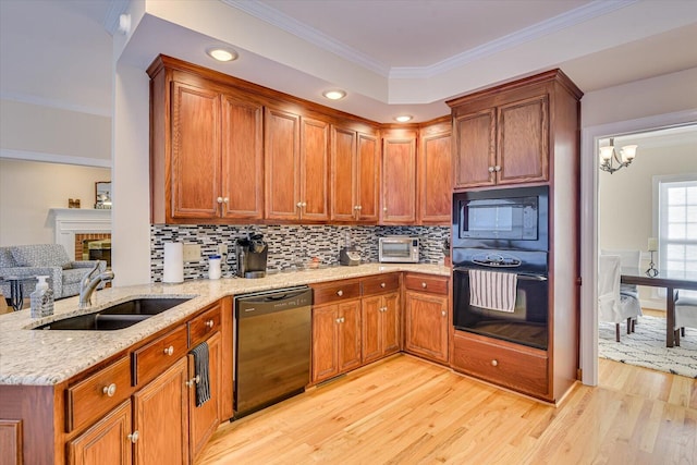 kitchen with a sink, light stone countertops, black appliances, light wood finished floors, and crown molding