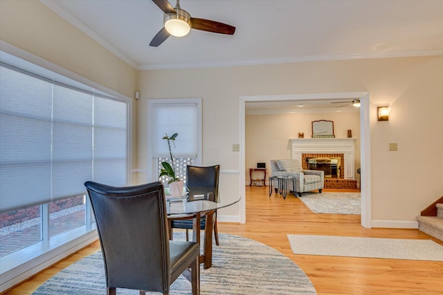 dining space featuring light wood-type flooring, a brick fireplace, baseboards, and crown molding