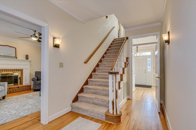 stairs with a brick fireplace, baseboards, ornamental molding, and wood finished floors