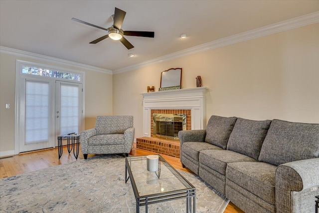 living room featuring ceiling fan, light wood-style flooring, a fireplace, french doors, and crown molding