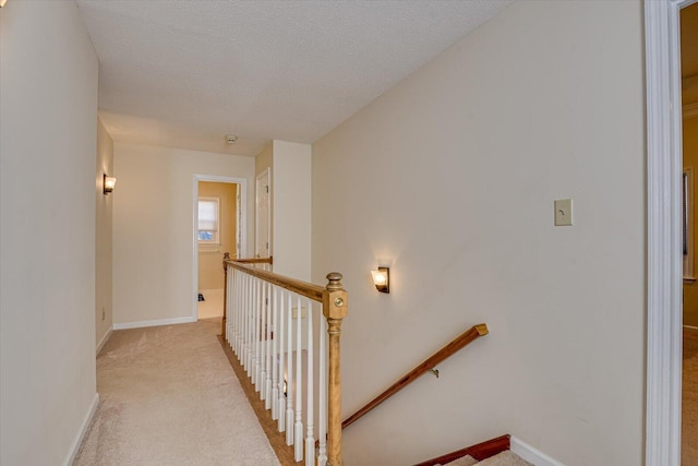 corridor featuring a textured ceiling, carpet flooring, an upstairs landing, and baseboards