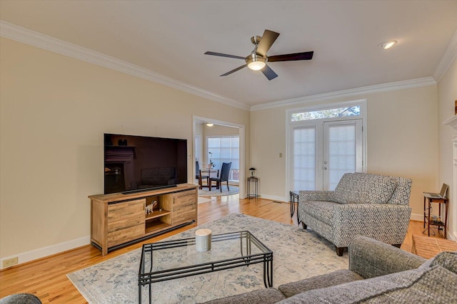 living area featuring light wood finished floors, baseboards, a ceiling fan, ornamental molding, and french doors