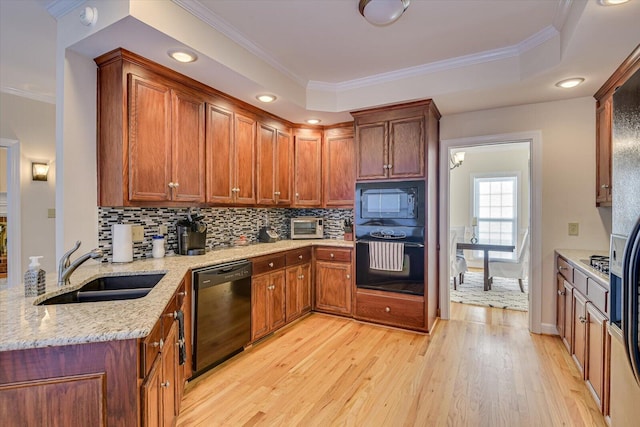 kitchen with a sink, ornamental molding, light wood-type flooring, light stone countertops, and black appliances