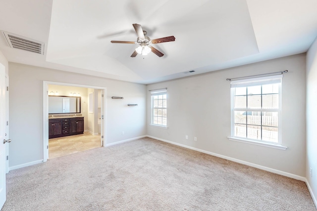 unfurnished bedroom featuring ceiling fan, light colored carpet, a tray ceiling, and connected bathroom