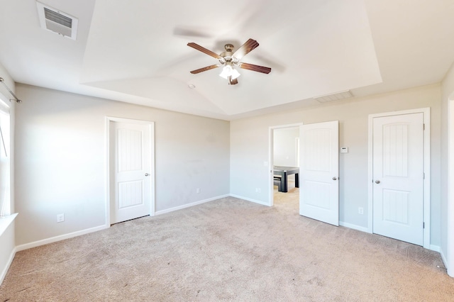 unfurnished bedroom featuring ceiling fan, light carpet, and a raised ceiling