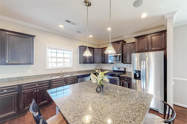 kitchen featuring stainless steel appliances, hanging light fixtures, a kitchen island, light stone counters, and sink