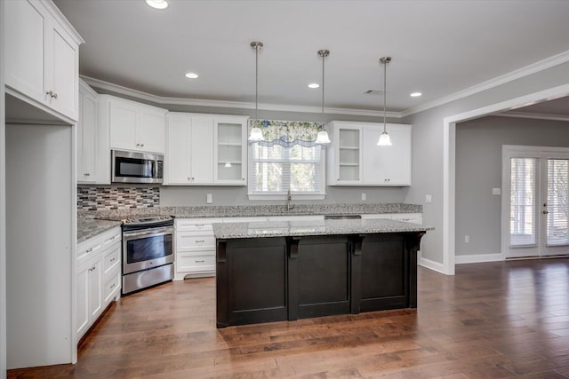 kitchen with white cabinets, hanging light fixtures, appliances with stainless steel finishes, a kitchen island, and light stone counters