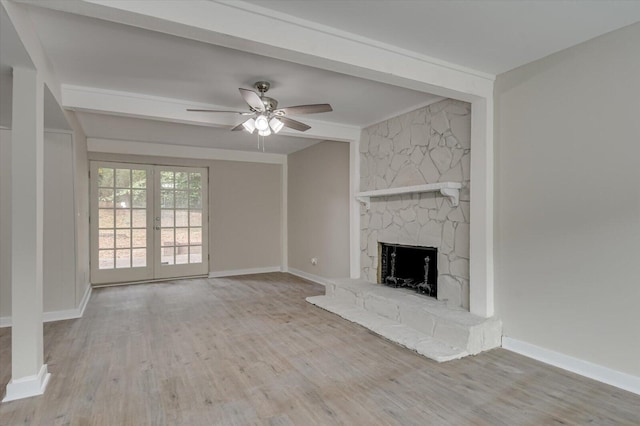 unfurnished living room with ceiling fan, a stone fireplace, wood finished floors, and baseboards