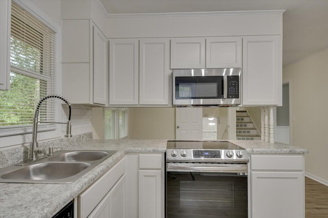 kitchen with crown molding, light countertops, appliances with stainless steel finishes, white cabinetry, and a sink