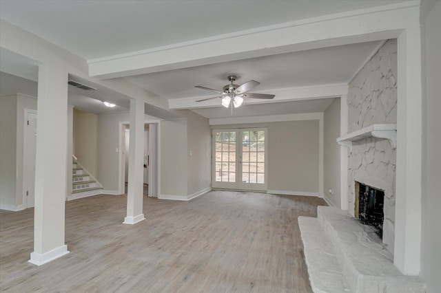 unfurnished living room with a premium fireplace, french doors, stairway, beam ceiling, and light wood finished floors