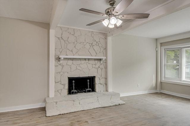 unfurnished living room featuring baseboards, ceiling fan, wood finished floors, a stone fireplace, and beam ceiling