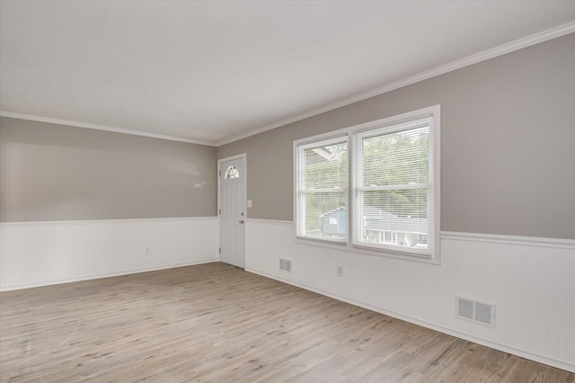 unfurnished room featuring a wainscoted wall, visible vents, wood finished floors, and ornamental molding