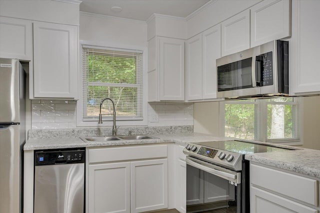 kitchen featuring decorative backsplash, ornamental molding, stainless steel appliances, white cabinetry, and a sink