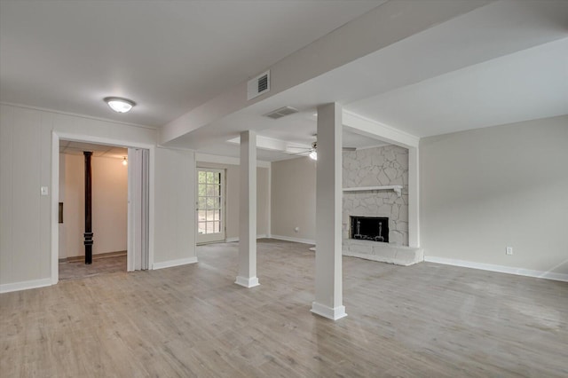 interior space featuring light wood-type flooring, visible vents, ceiling fan, and a stone fireplace