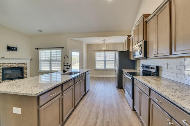 kitchen with a center island with sink, light wood finished floors, a sink, stainless steel appliances, and backsplash