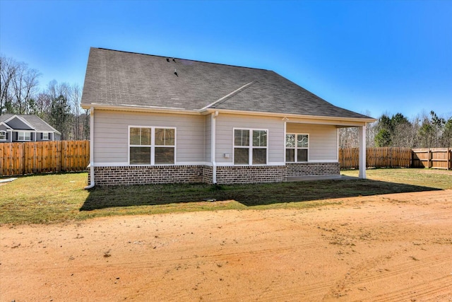 rear view of property featuring a shingled roof, fence, brick siding, and a lawn