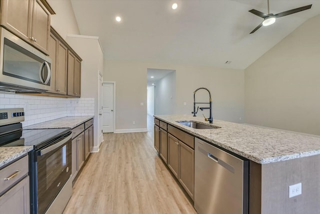 kitchen featuring a kitchen island with sink, a sink, backsplash, stainless steel appliances, and light wood-style floors