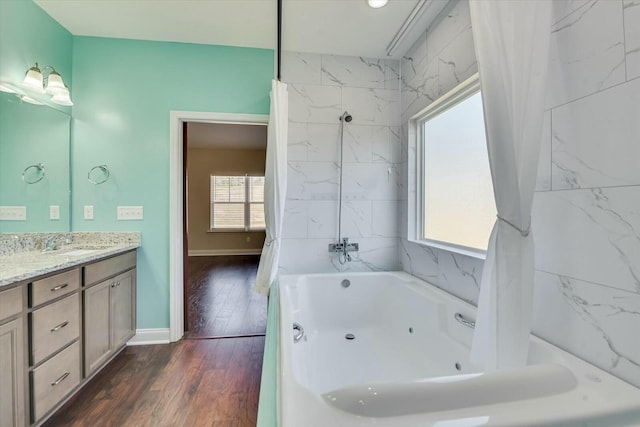 full bathroom with a tub with jets, vanity, baseboards, and wood finished floors