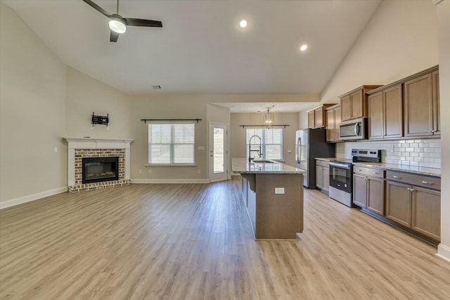 kitchen with light wood-style flooring, light stone counters, open floor plan, appliances with stainless steel finishes, and ceiling fan