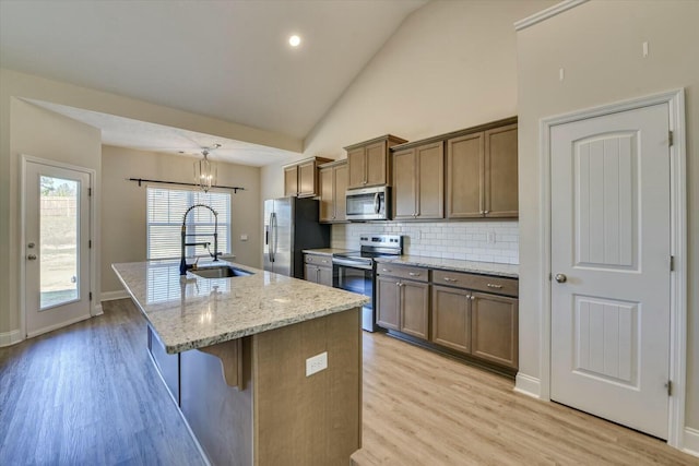 kitchen featuring a kitchen island with sink, appliances with stainless steel finishes, light wood-type flooring, and a sink