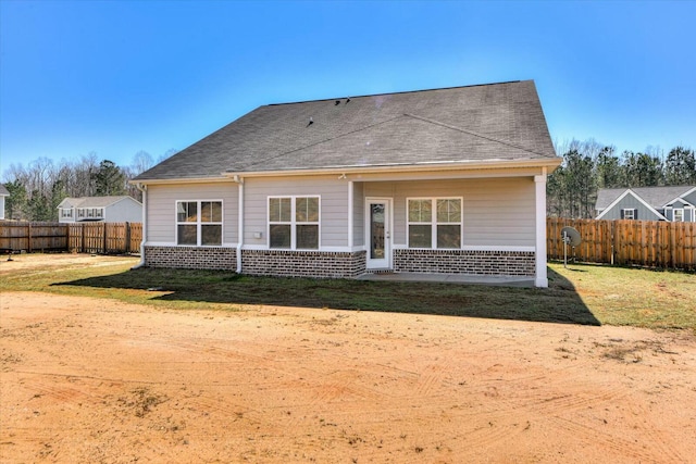 rear view of house featuring brick siding, a shingled roof, and fence