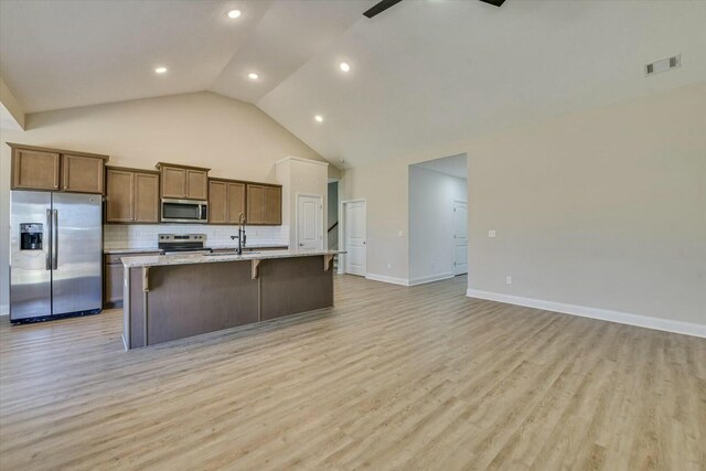 kitchen with a center island with sink, visible vents, light wood-style flooring, stainless steel appliances, and decorative backsplash