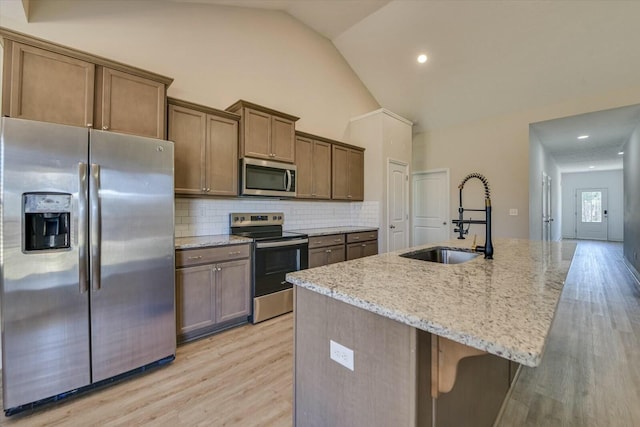 kitchen with light wood-style flooring, a sink, tasteful backsplash, stainless steel appliances, and light stone countertops