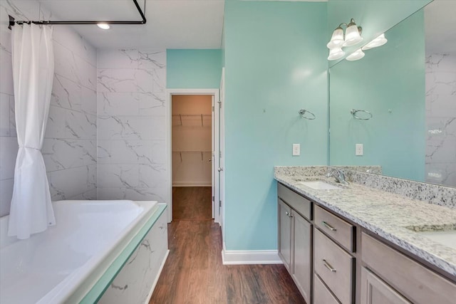 full bathroom with a spacious closet, double vanity, a bathtub, wood finished floors, and a sink