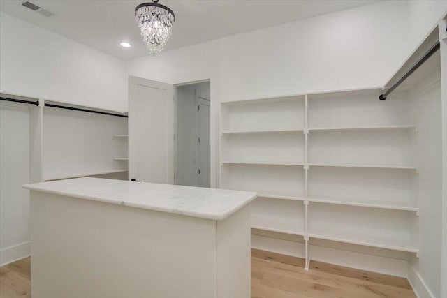 spacious closet with light hardwood / wood-style flooring and a notable chandelier